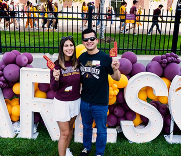 Two Carlson School alumni posing in front of Carlson block letters at a homecoming tailgate.